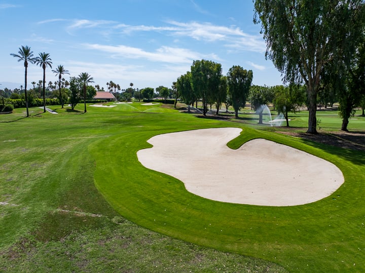 View of the bunker on Hole 3 at The Springs Country Club, with the green visible in the background beyond the sand trap and fairway.