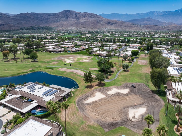 Same view of Hole 5 green at The Springs Country Club during demolition, with a tractor actively removing turf and reshaping the area.